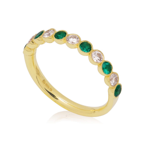 An 18ct yellow gold emerald and diamond millegrain set half eternity ring, containing eleven stones.